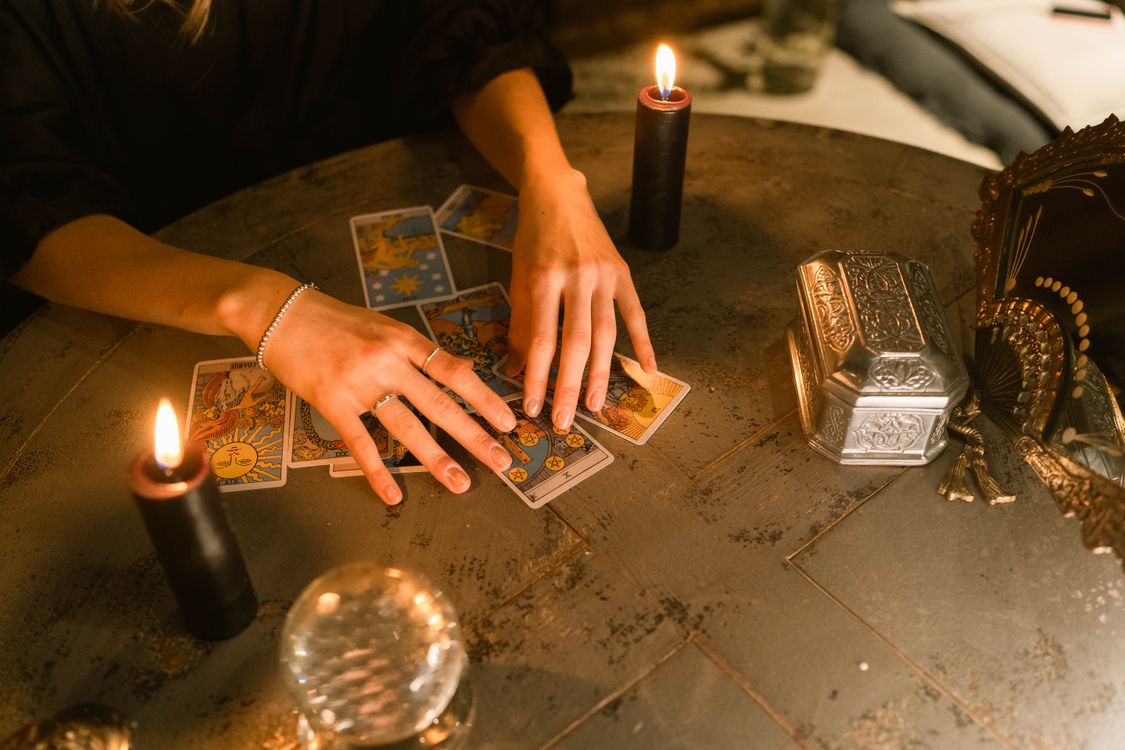 Manos de una vidente colocando cartas de tarot sobre una mesa con velas encendidas
